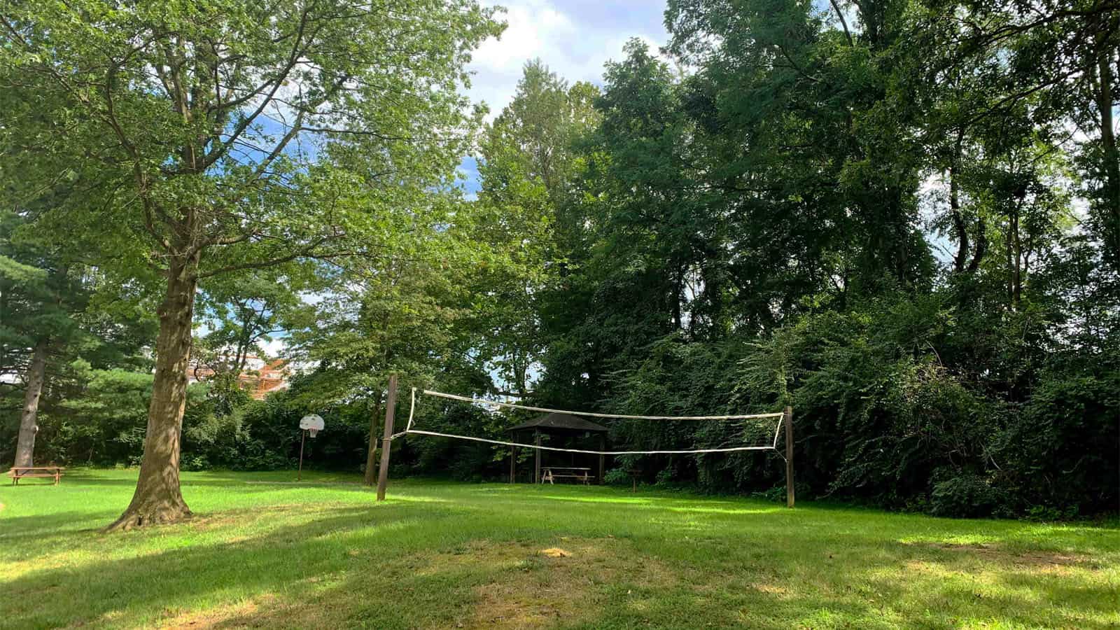 Sandstone Care's Reston Rehab Centers outdoor area with green trees, a grassy field featuring a volleyball net, and a picnic bench under the shade