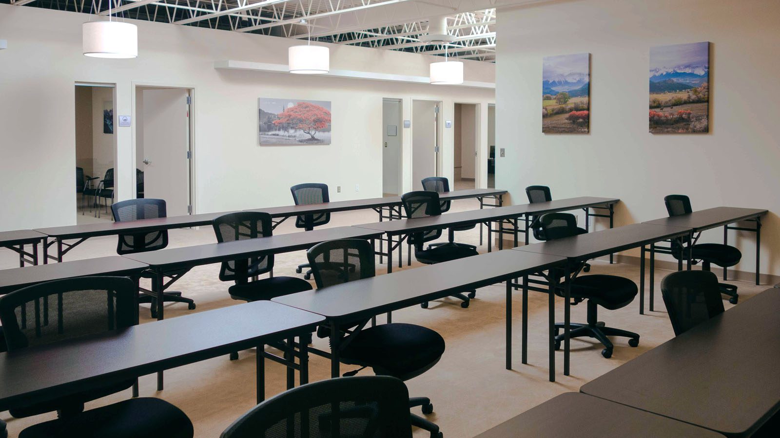 Spacious vocational room at Sandstone Care's Reston Rehab Center with rows of black chairs and desks, adorned with landscape paintings on the wall.