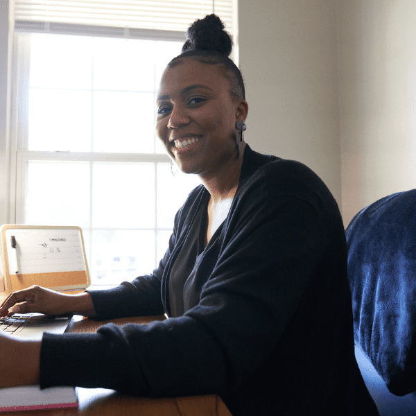 Black woman sitting and smiling at a computer.