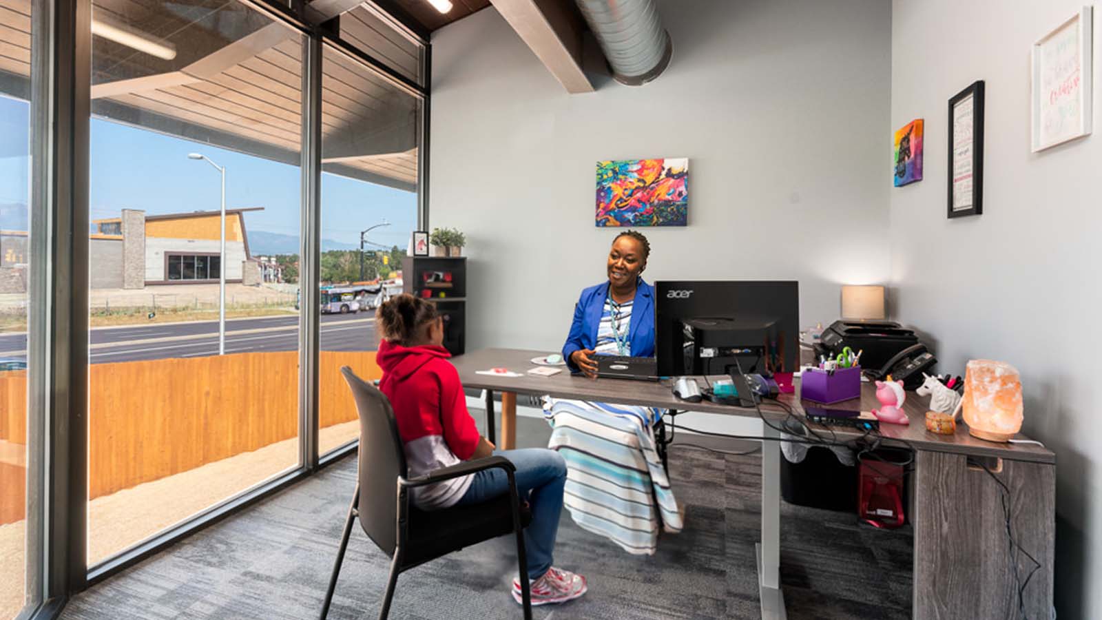 A smiling clinician sits across a desk from a teenage girl in the Colorado Springs office.