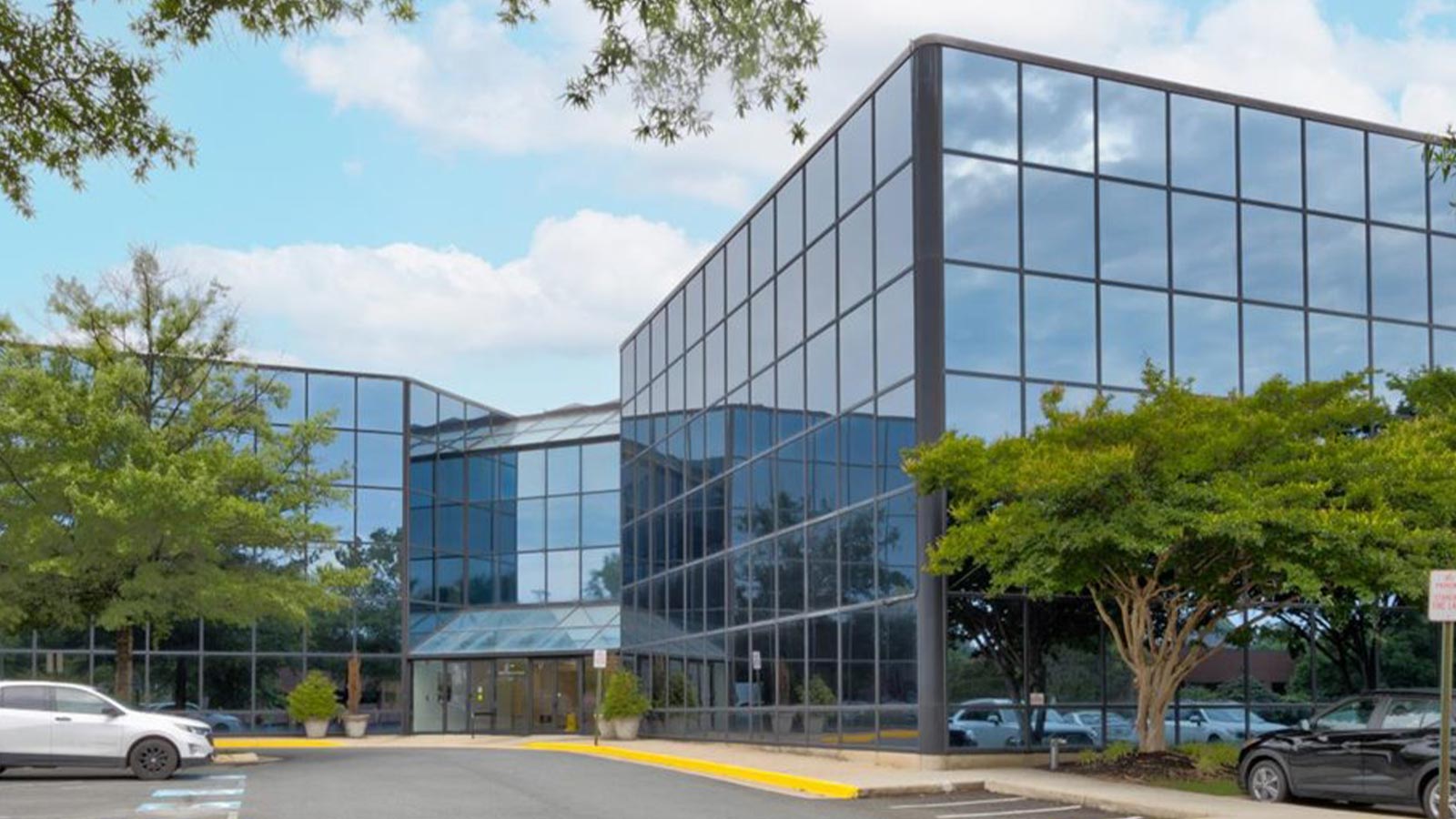 A modern building with reflective glass surrounded by green trees under a cloudy sky.