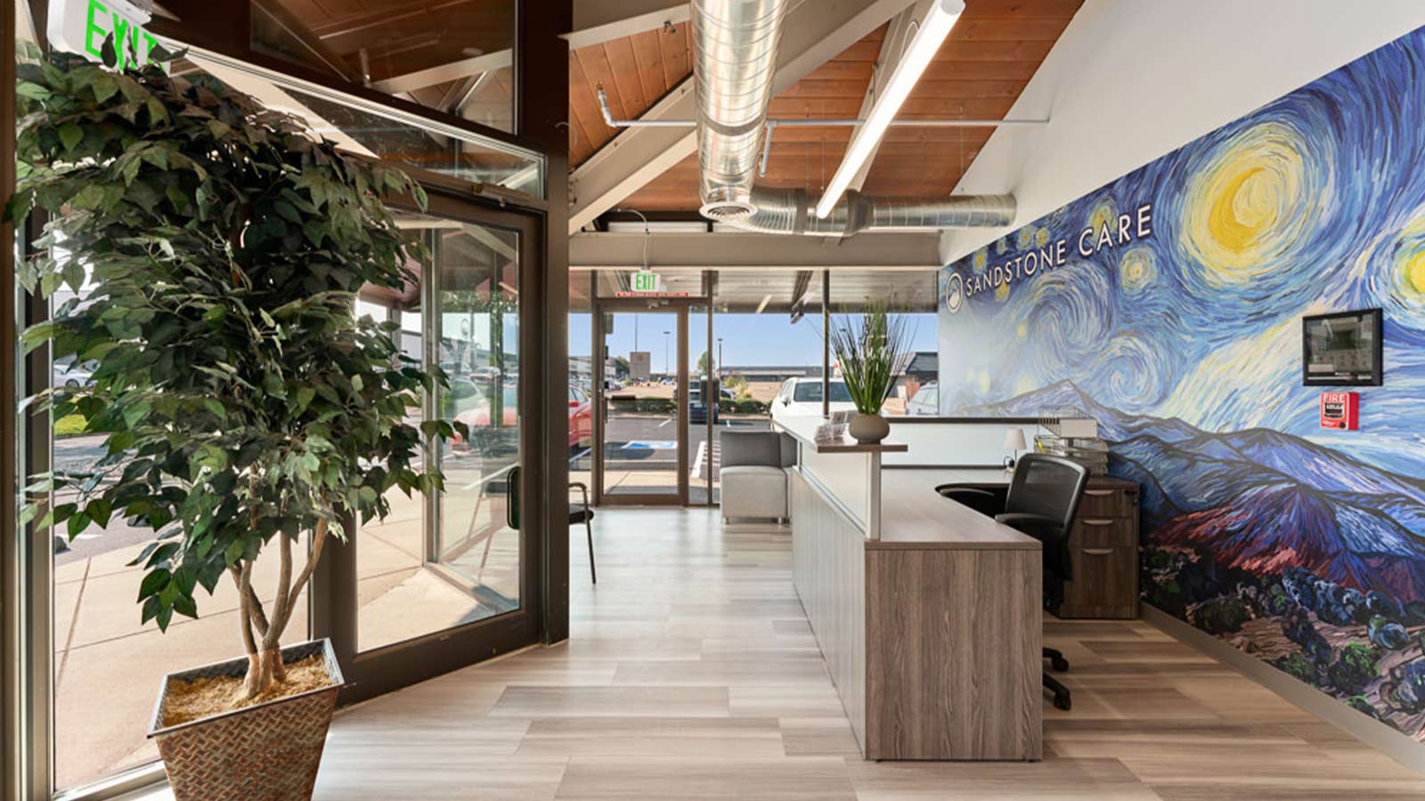 A modern lobby area with a large tree, beamed ceilings, and a vibrant wall mural depicting a landscape.