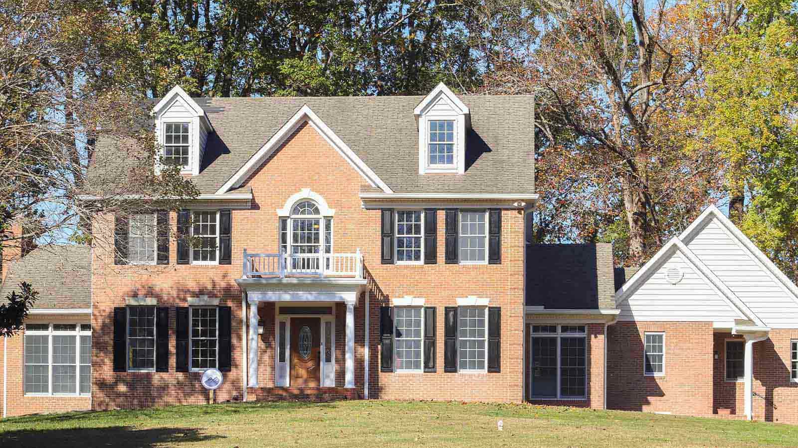 A two-story brick house with multiple windows, gabled roofs, and a front yard