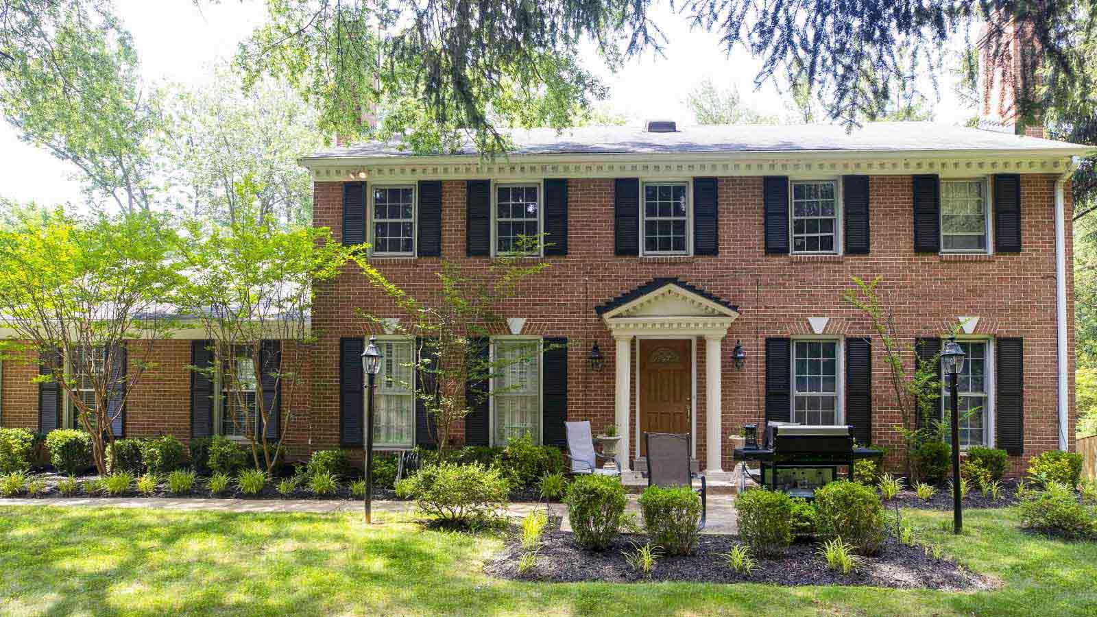 A two-story brick house with green landscaping and a clear blue sky.