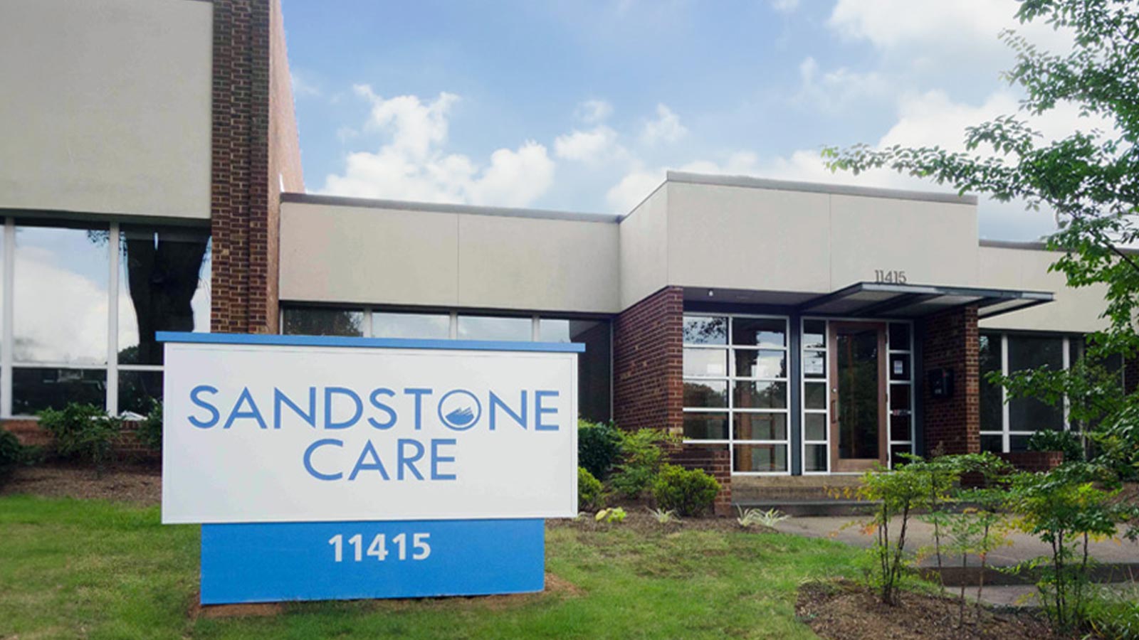 A two-story building with a mix of brick and beige facade features a prominent "Sandstone Care" sign at the entrance.