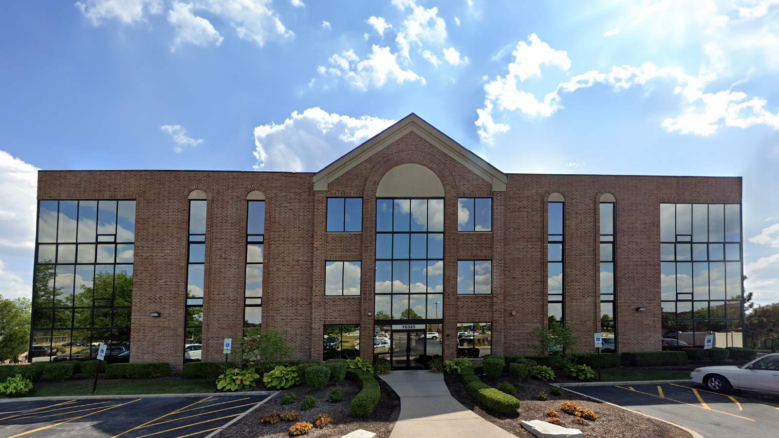A symmetrical, brick office building with a central arched entrance and large reflective windows, under a blue sky.