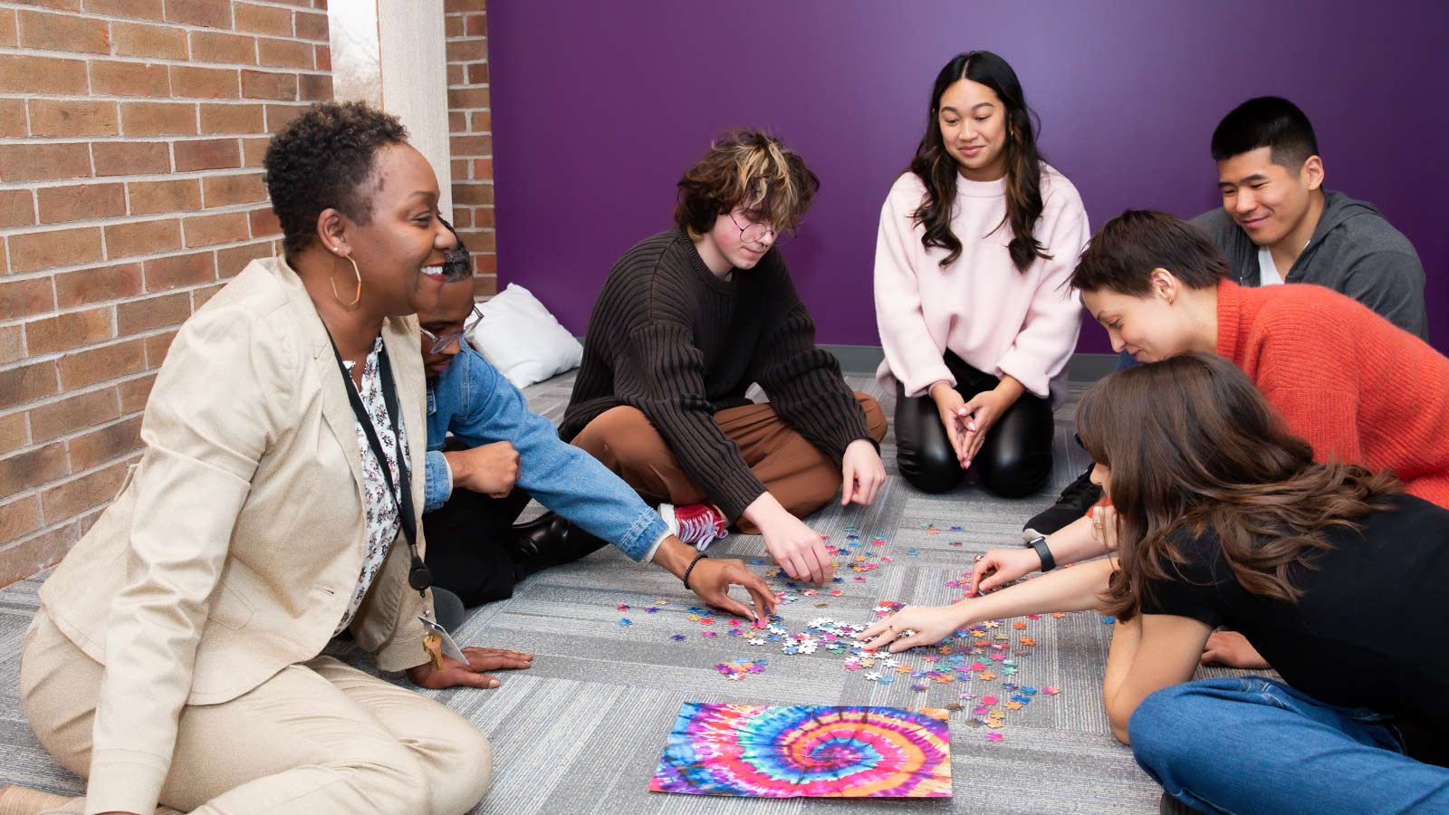 A group of diverse individuals sitting on the floor, engaging in a collaborative puzzle activity.