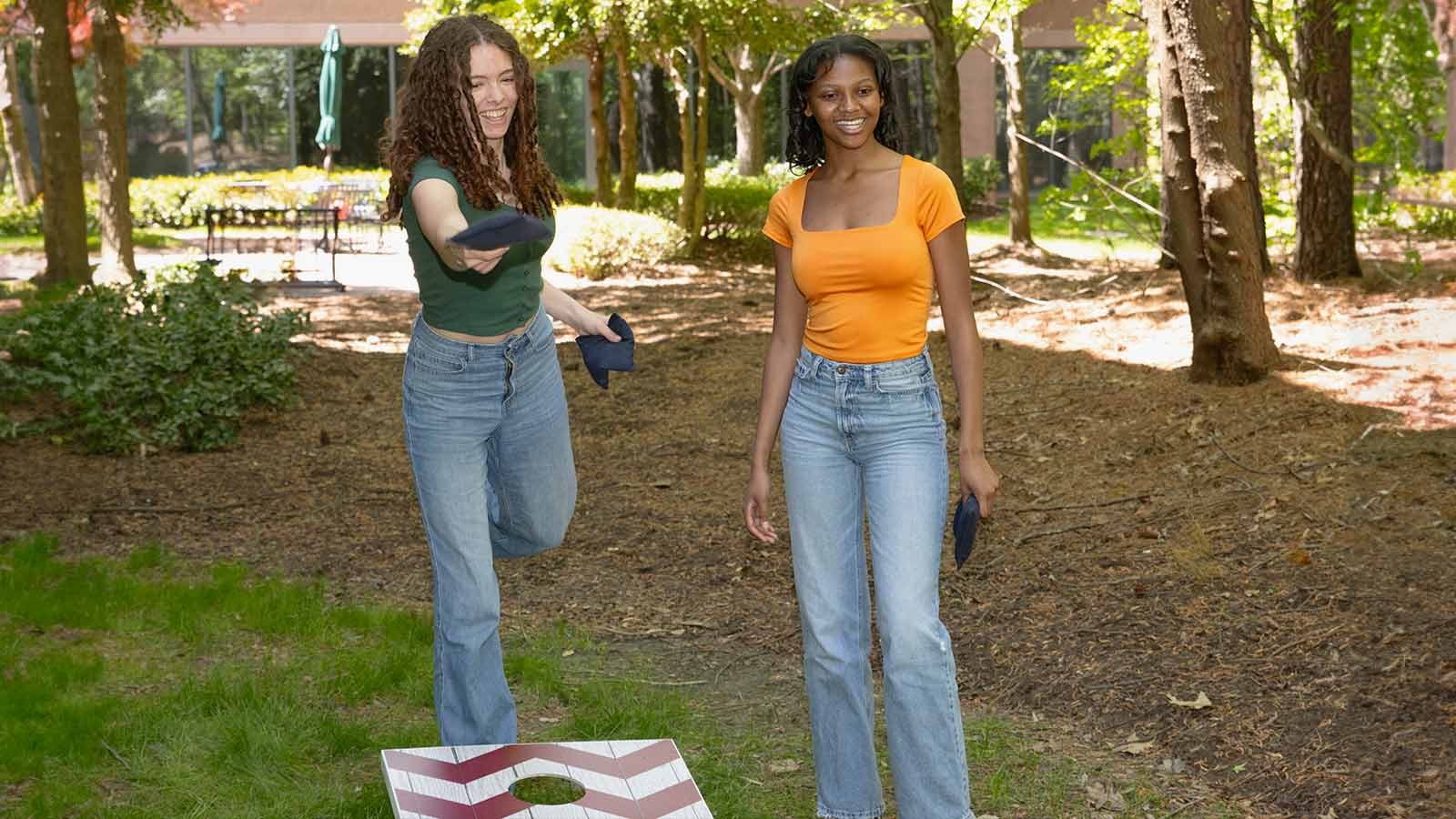 Two teenagers playing a game of cornhole.