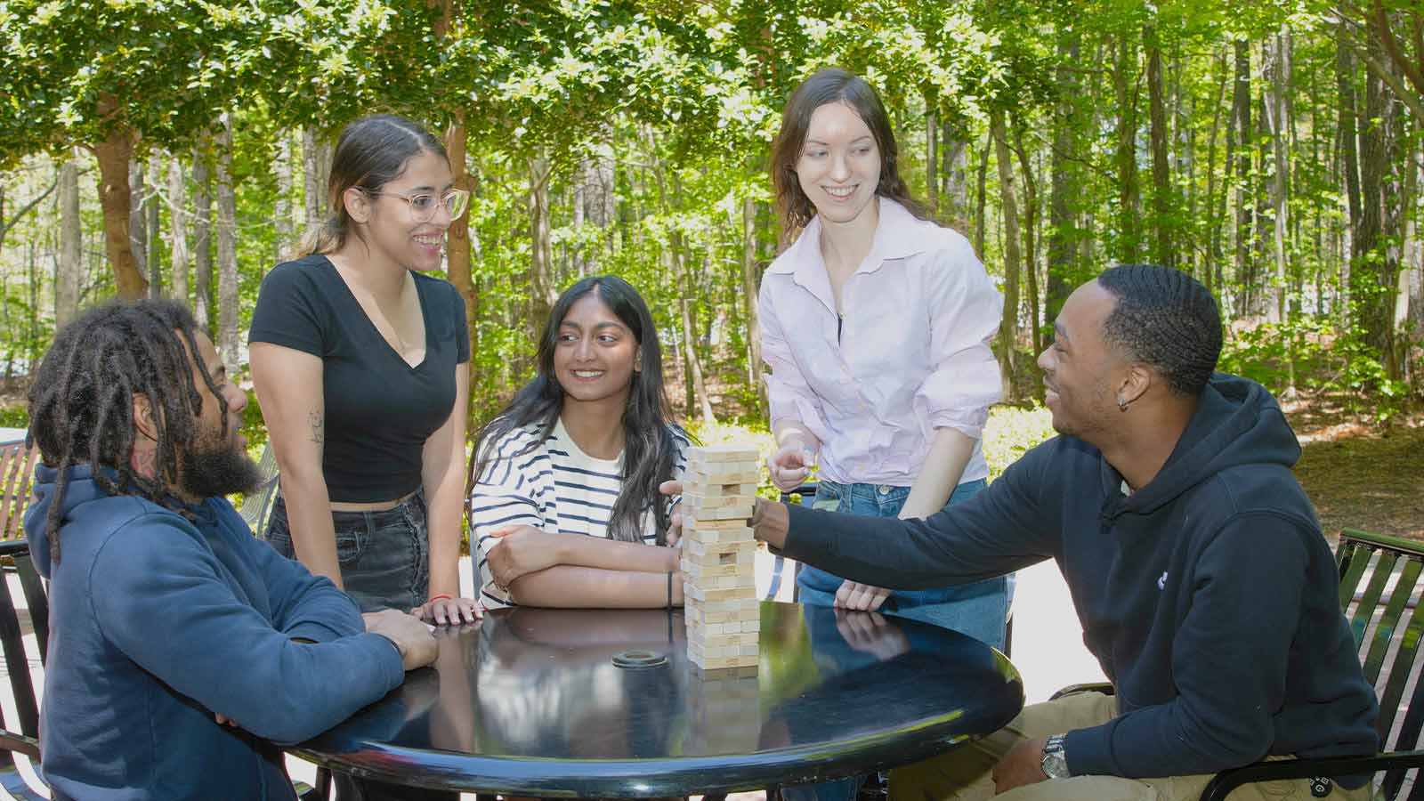 Young adults playing a game of Jenga on an outdoor table.