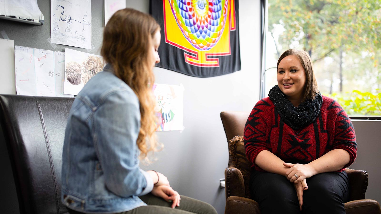 Two women having a conversation in an office with artwork on the wall.