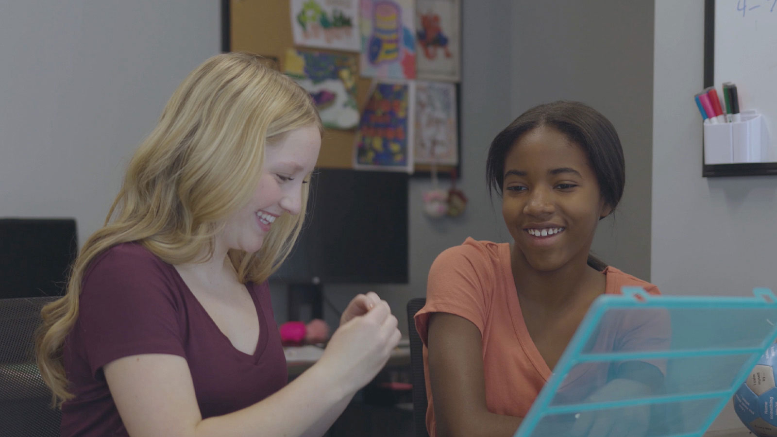 Two teenage females smiling and interacting over a learning activity in a therapy session.