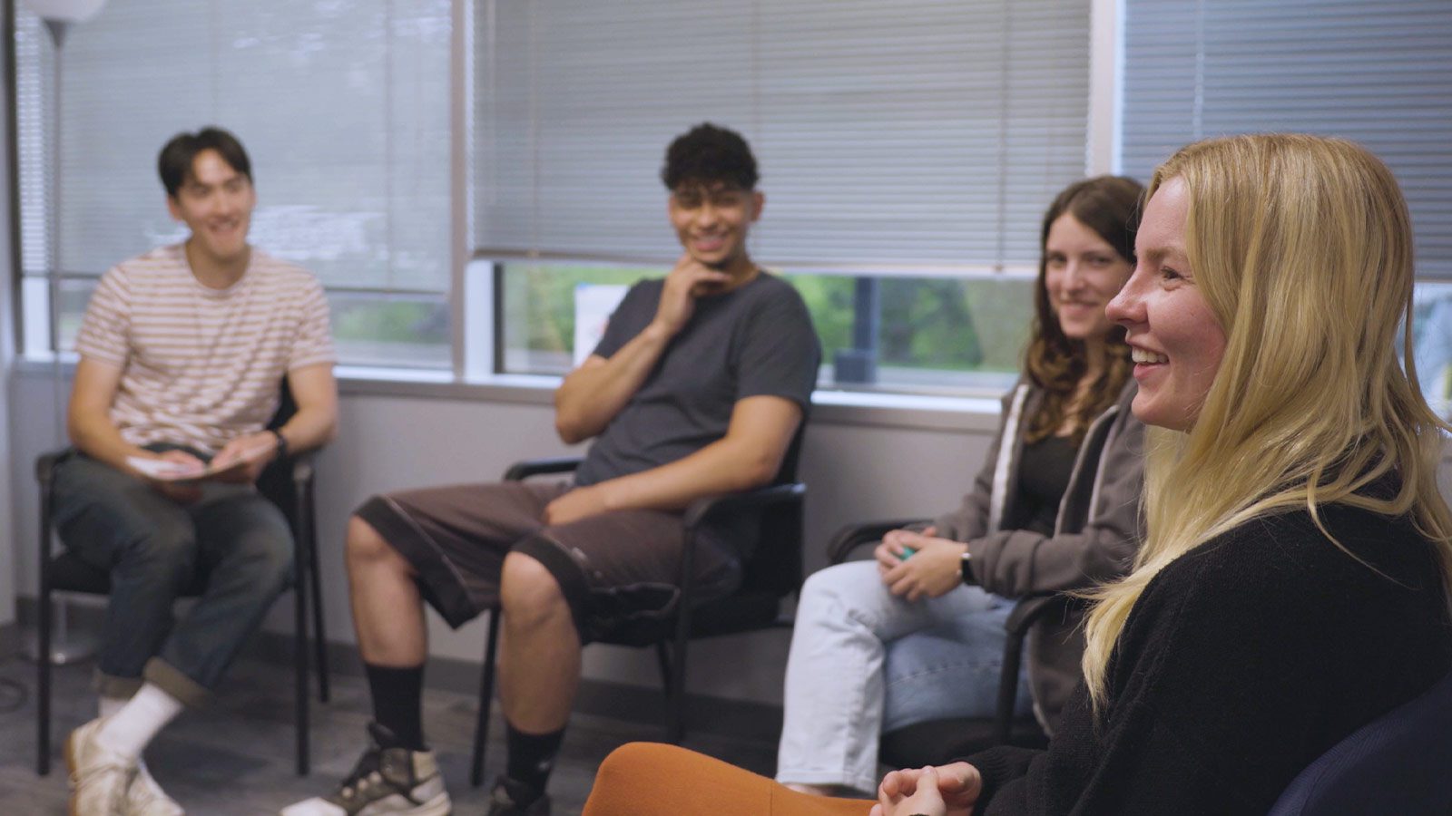 A group of smiling individuals in a casual office setting, engaging in a lively discussion.