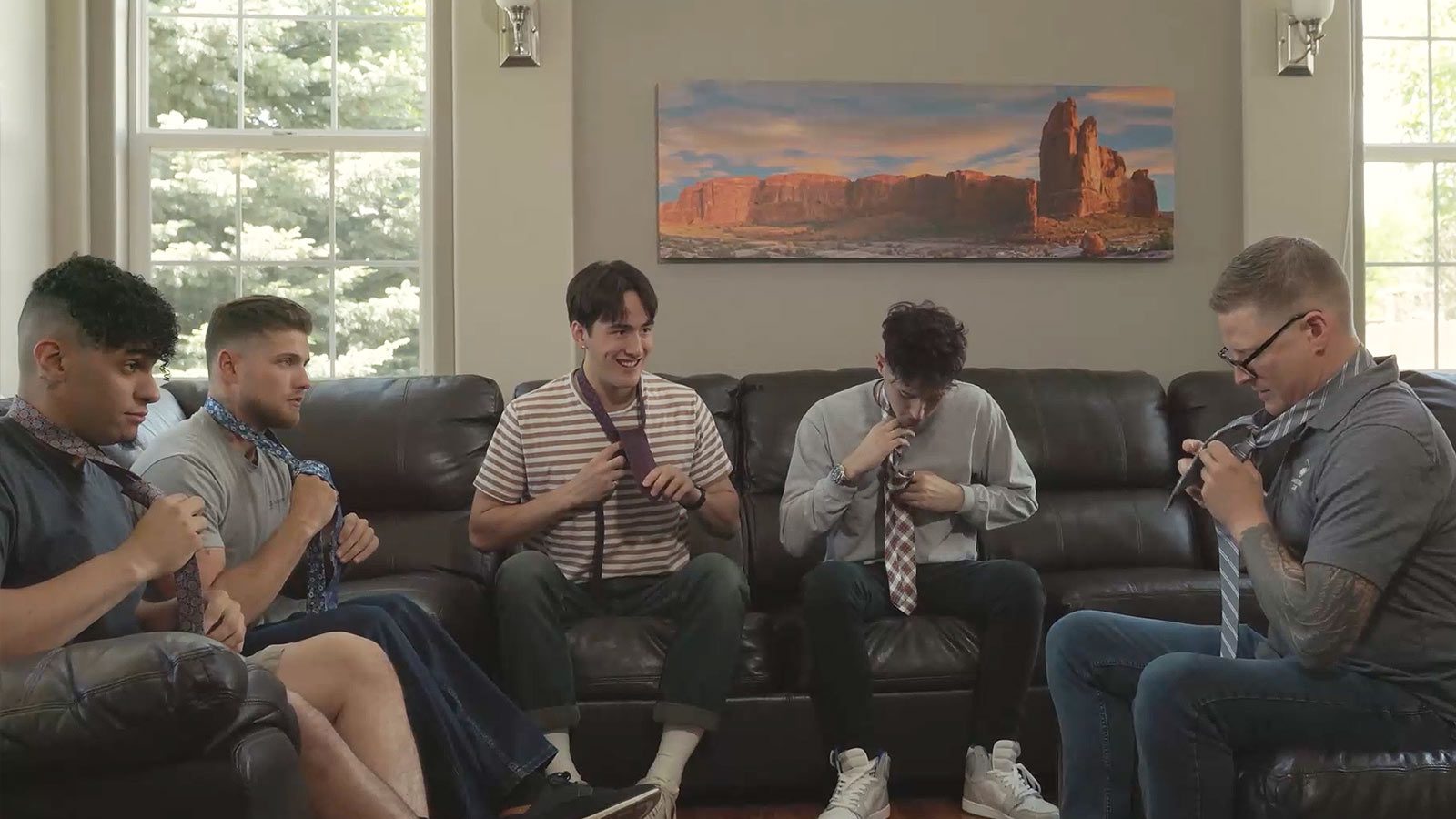 several men sitting on a couch in a living room with a painting on the wall