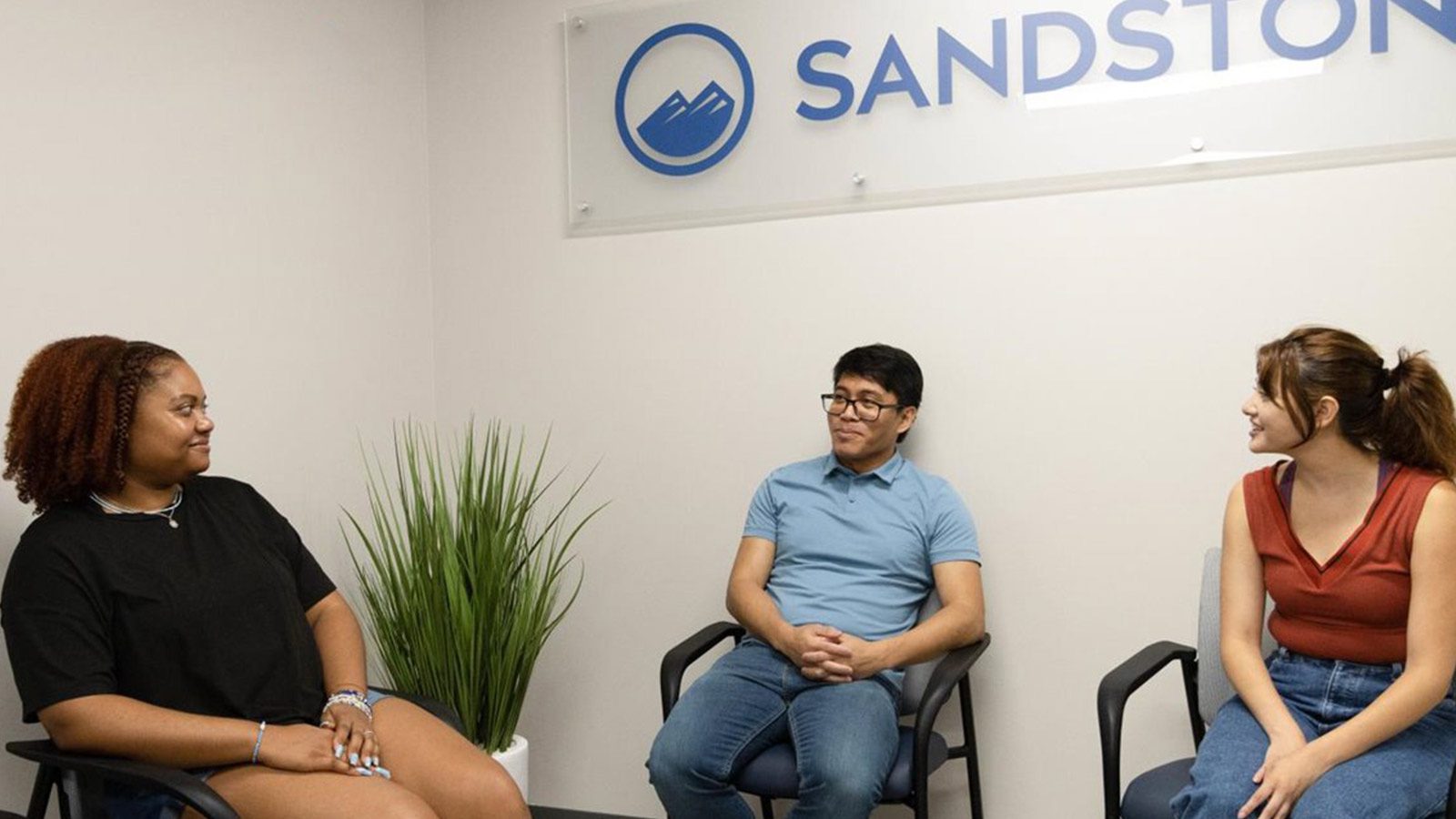 Three people sitting in a waiting room engaged in conversation.