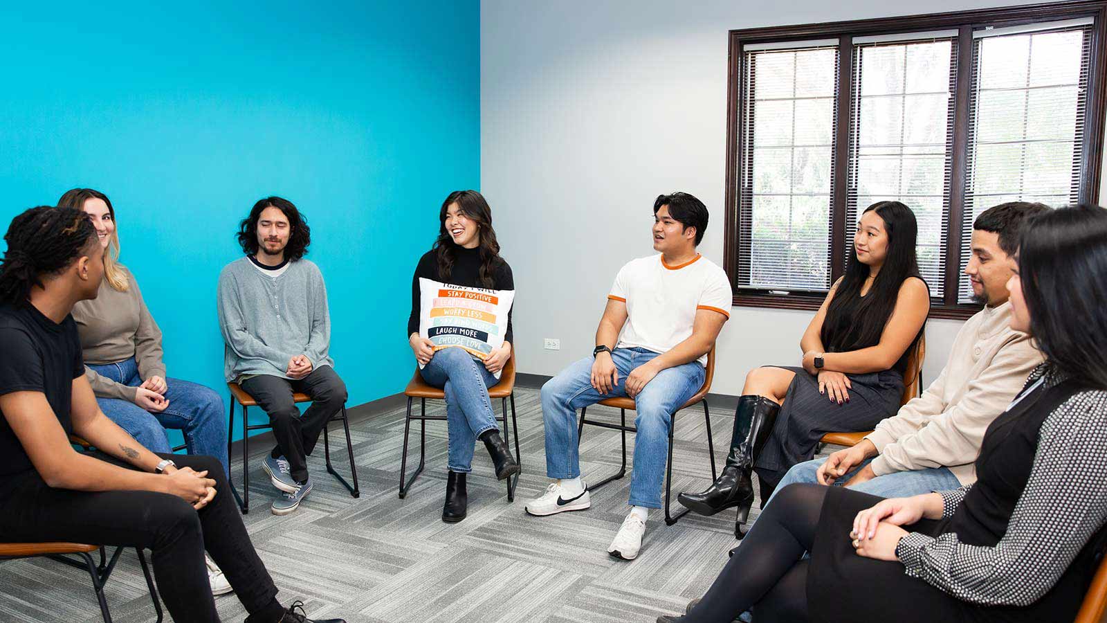 A group of individuals sitting in chairs forming a circle for group therapy in a room with bright blue walls.