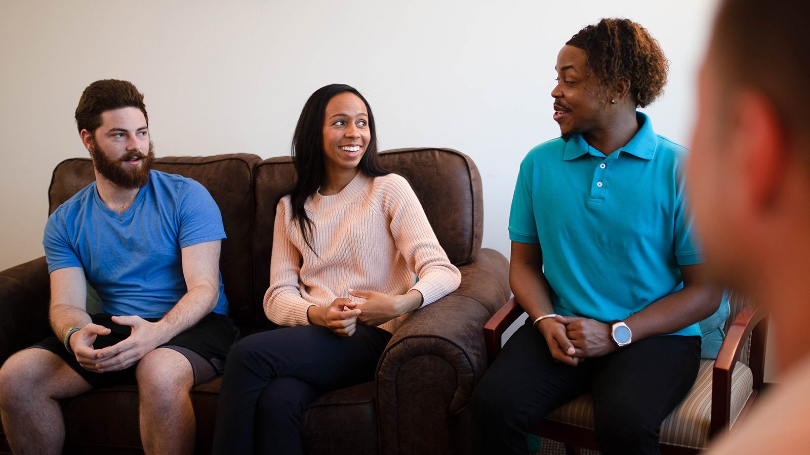 Three people engaging in a friendly conversation on a sofa in a warmly lit room.