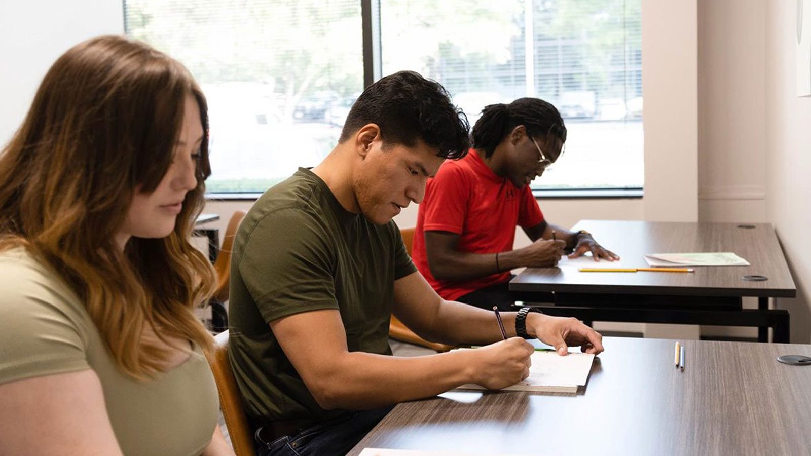 Three students focused on writing notes at desks in a classroom setting.