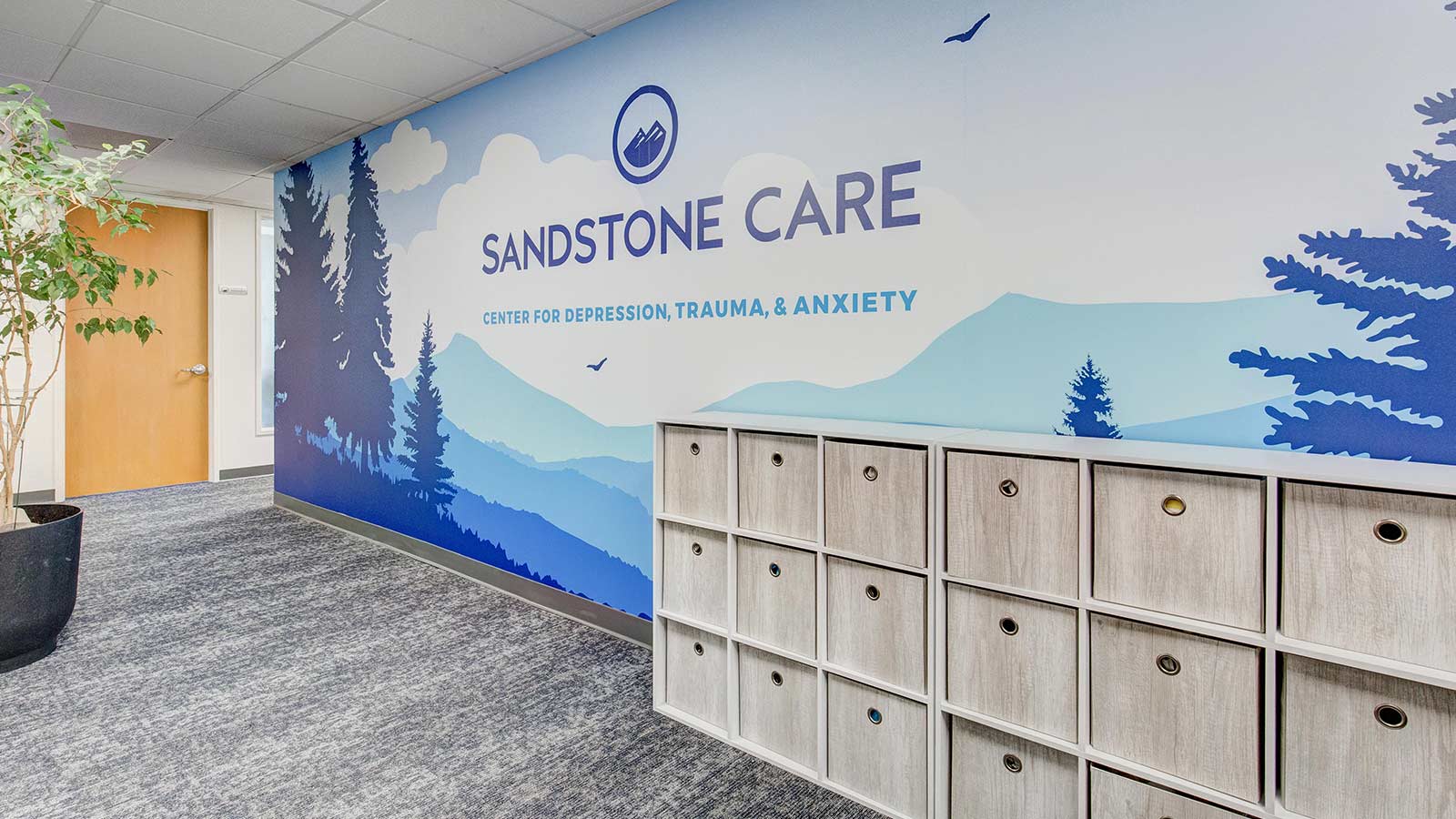Wall mural with mountain scenery and the Sandstone Care logo in a hallway.