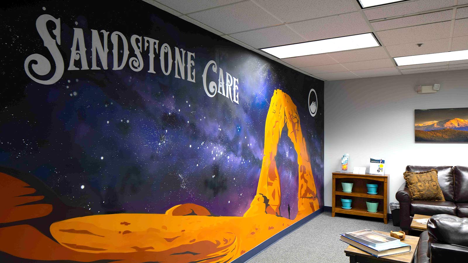 A large mural of a starry sky and sandstone arch with the words "Sandstone Care" on an interior wall of a waiting area.