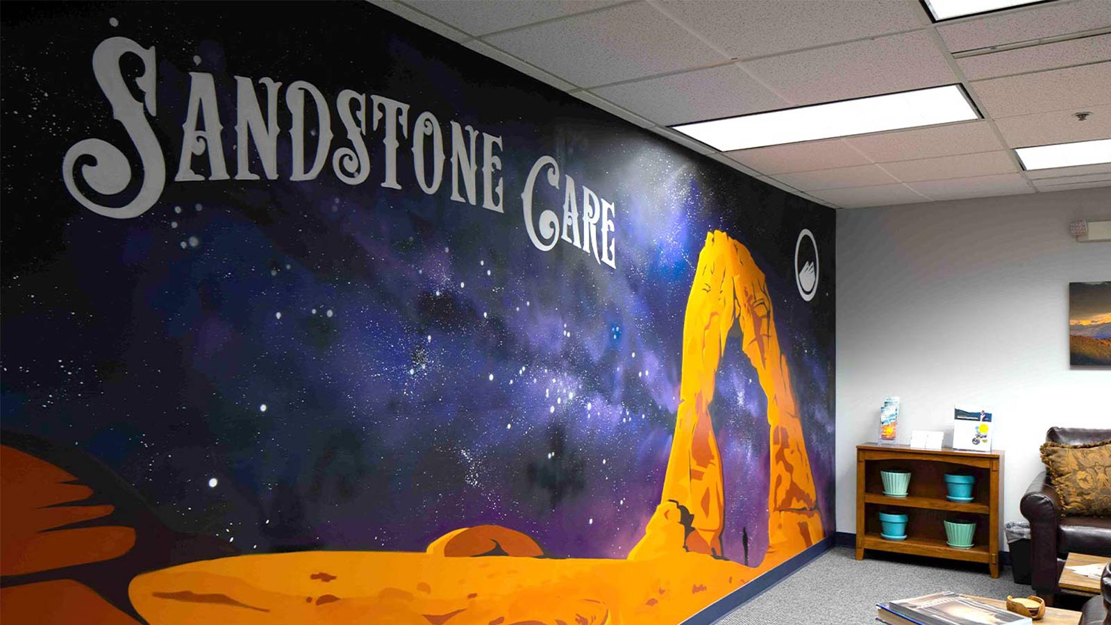 A large mural of a starry sky and sandstone arch with the words "Sandstone Care" on an interior wall of a waiting area.