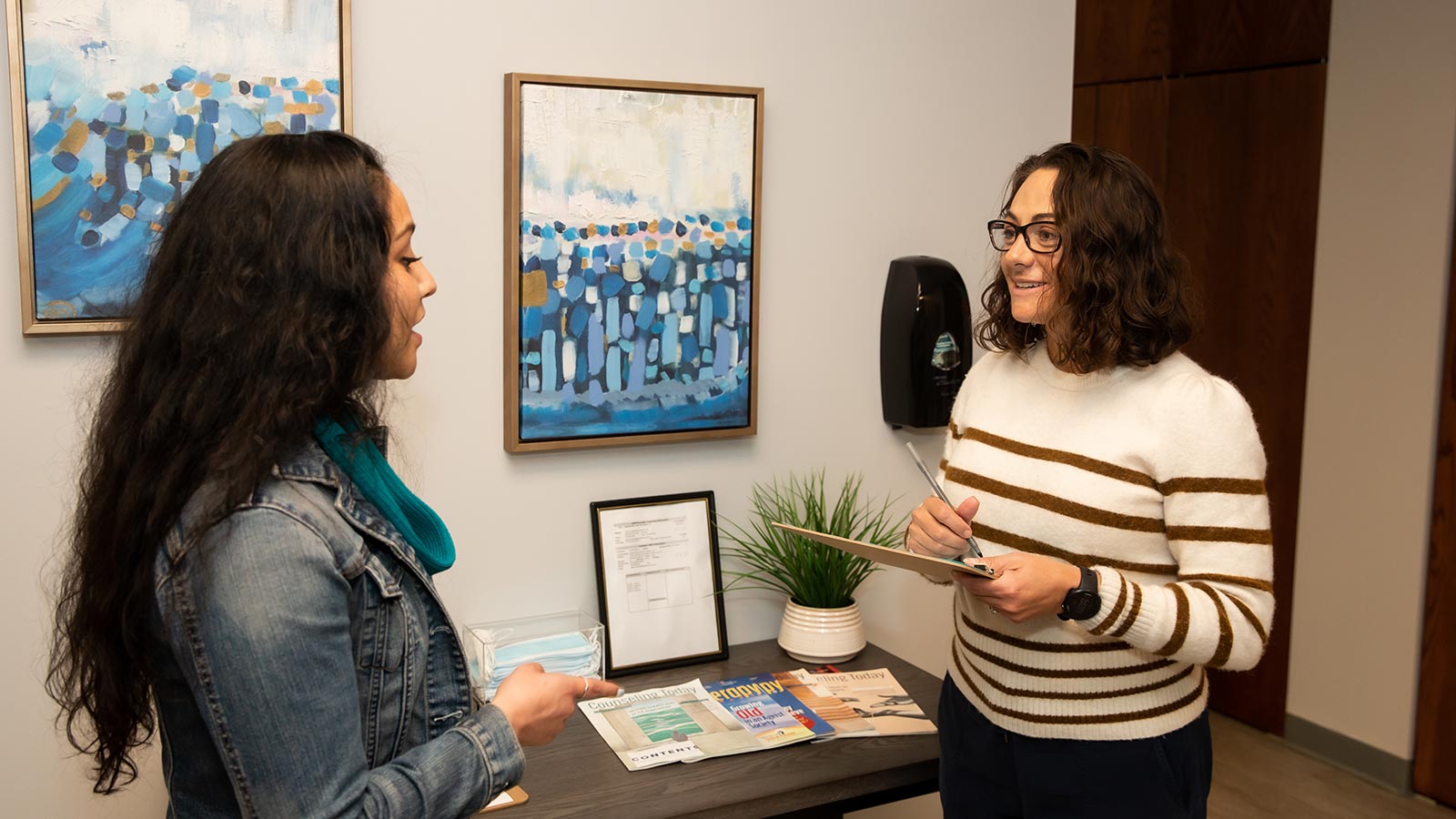 Two people exchanging admissions paperwork and a conversing in an open office space.