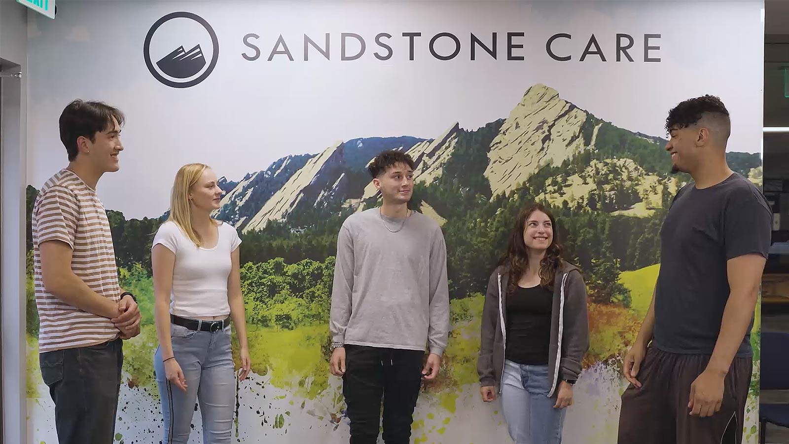 Four young people smiling and chatting beside a backdrop featuring mountain scenery.