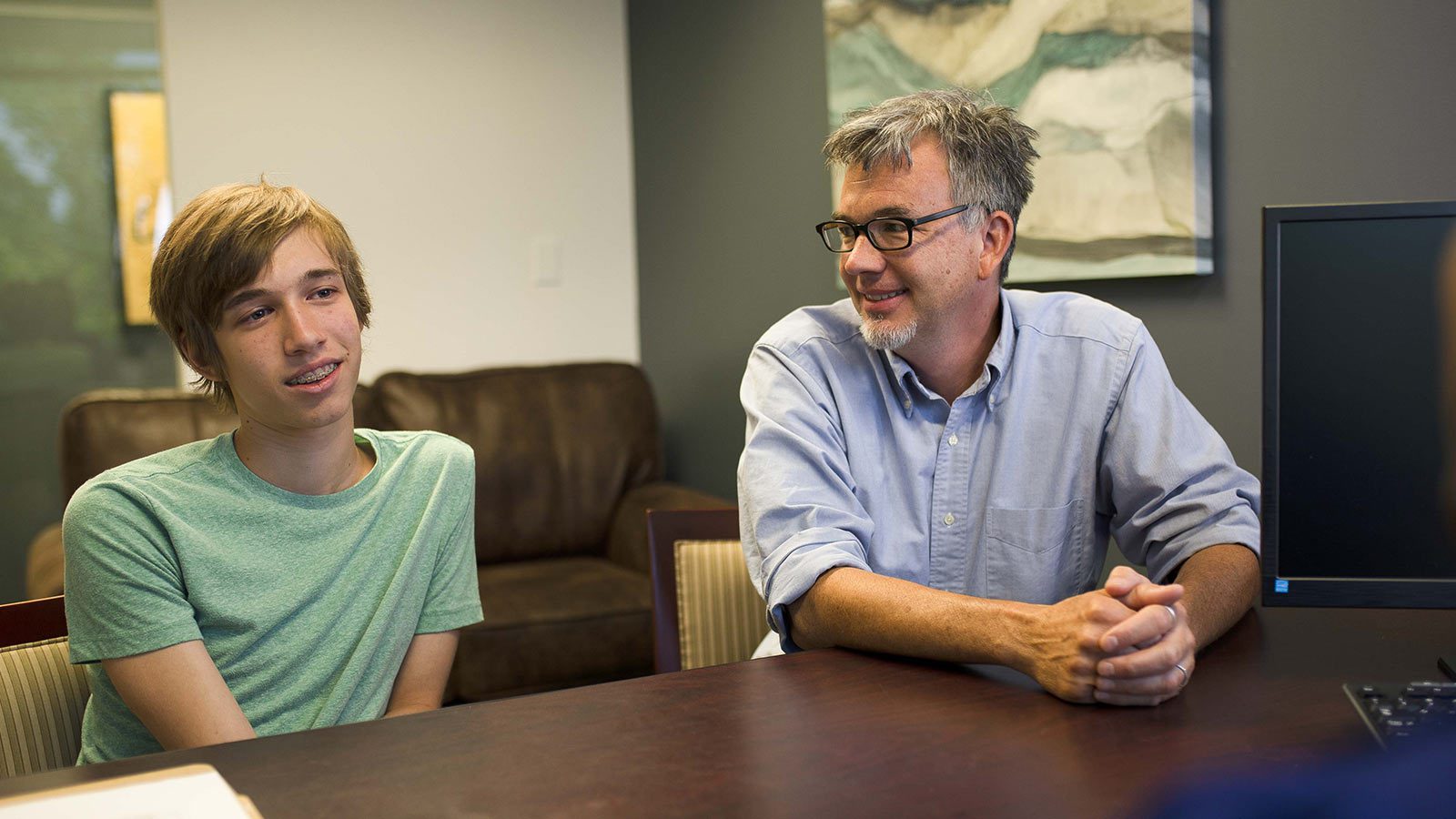 A teenager and their parent sitting across from each other, engaged in a conversation in an office setting.