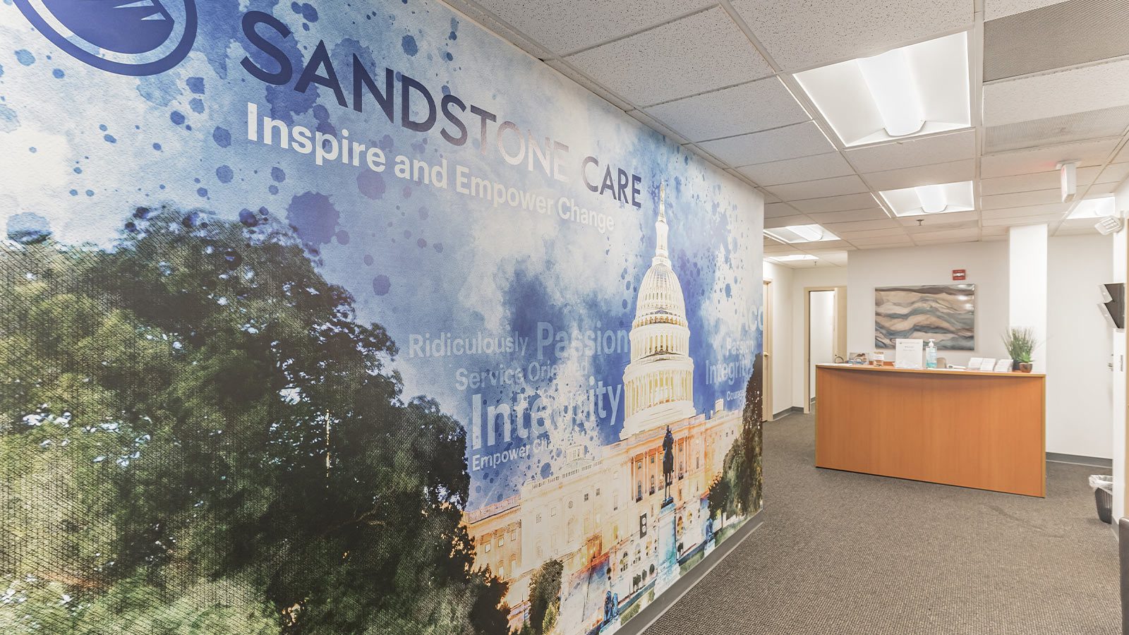 An office lobby with a large wall mural featuring a cityscape and branding for Sandstone Care.
