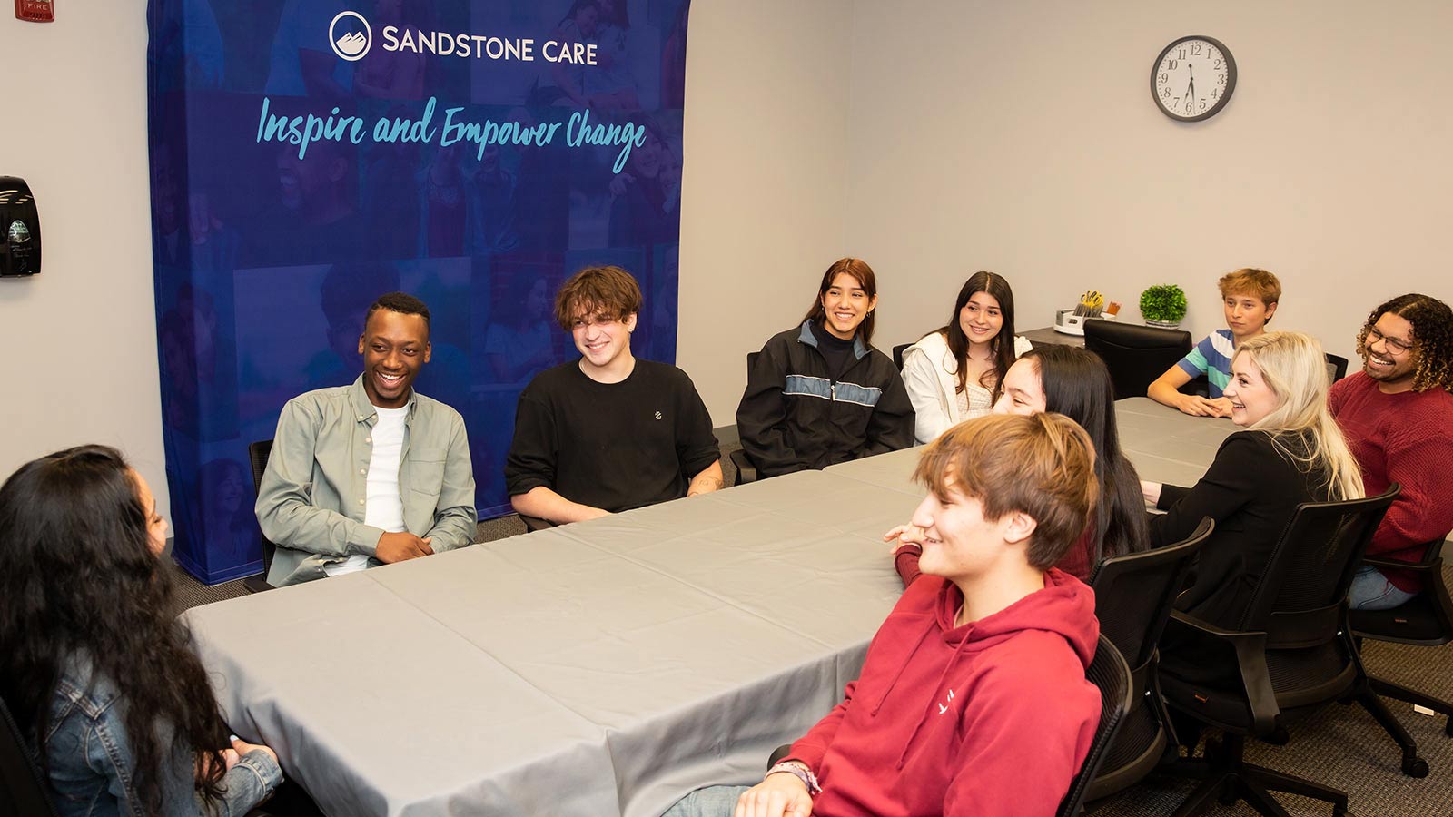 A lively group meeting with young adults and a Sandstone Care banner in the background.
