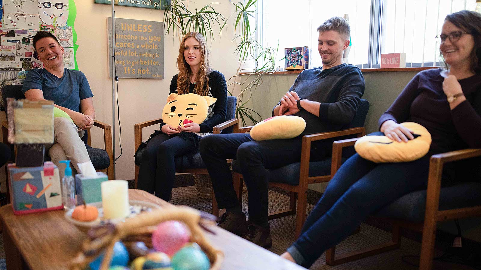 A group therapy session where participants are holding emoticon pillows and sharing a light-hearted moment.