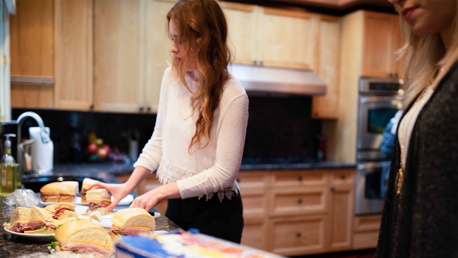 A moment in the kitchen with two women preparing sandwiches.