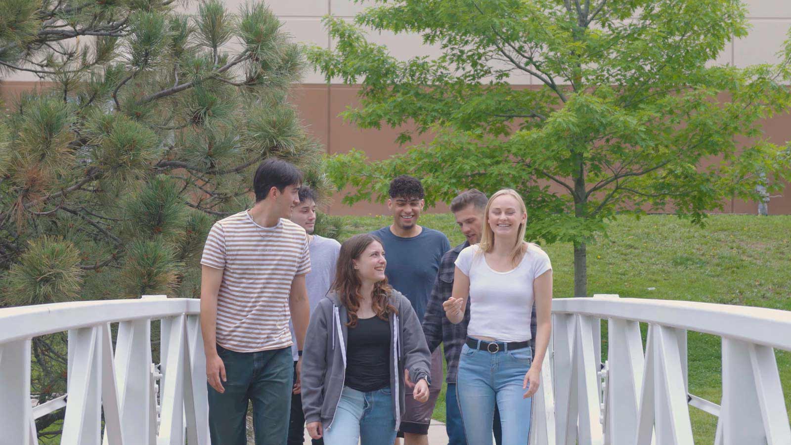 A group of young adults walking and chatting on an outdoor bridge in a tranquil environment.
