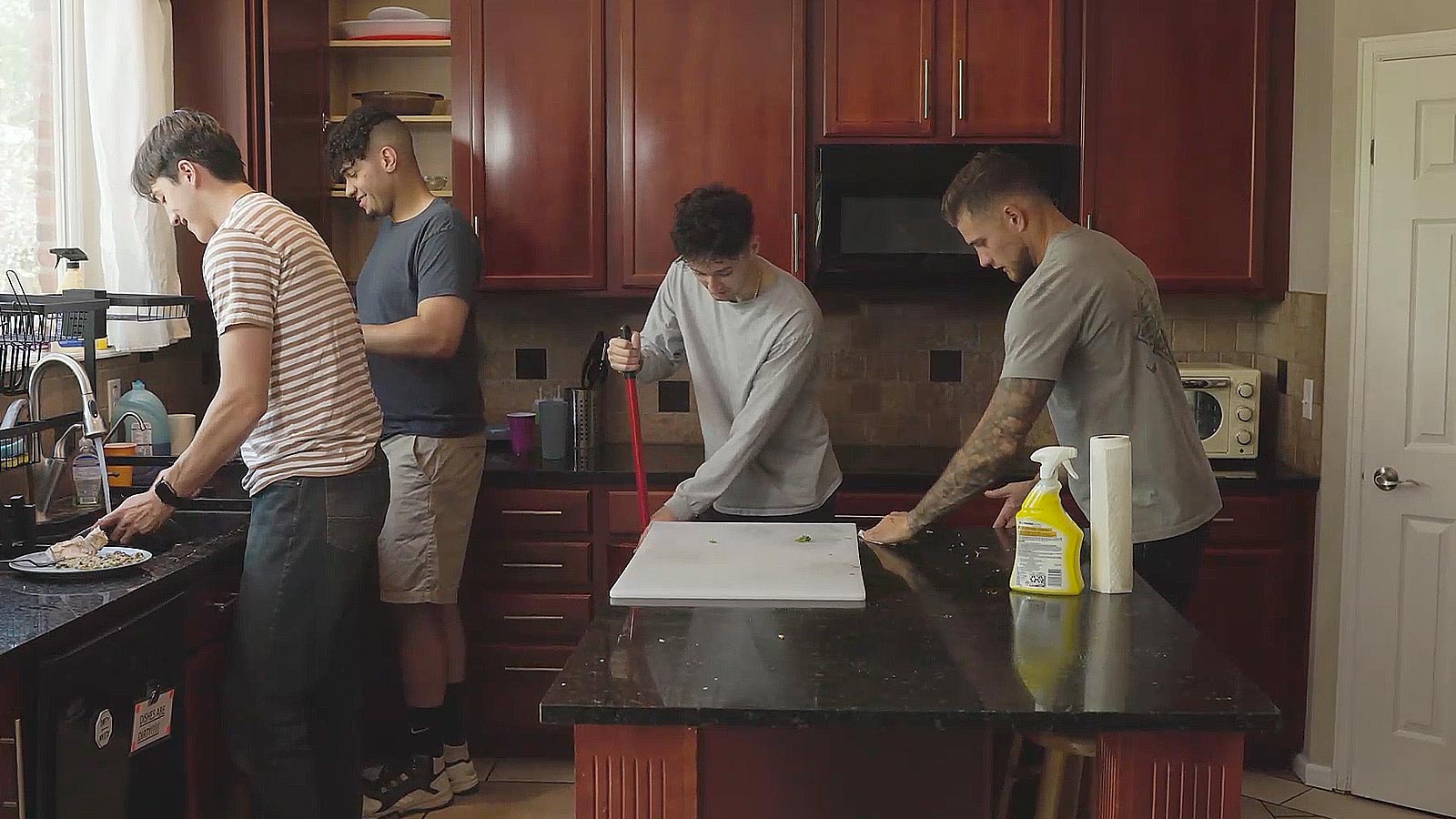Four men preparing food and cleaning in a modern kitchen.