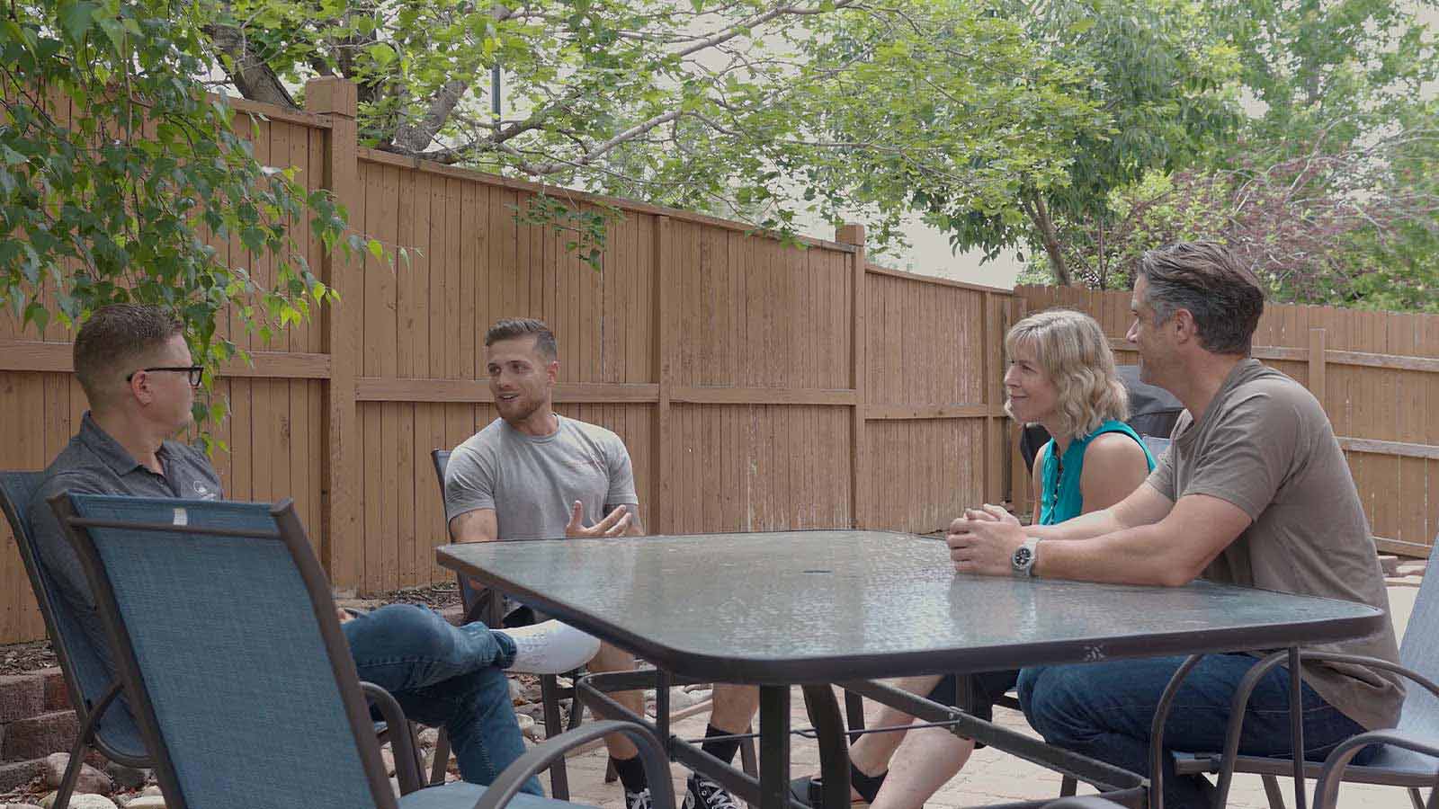 Four people engaging in conversation at an outdoor patio table.