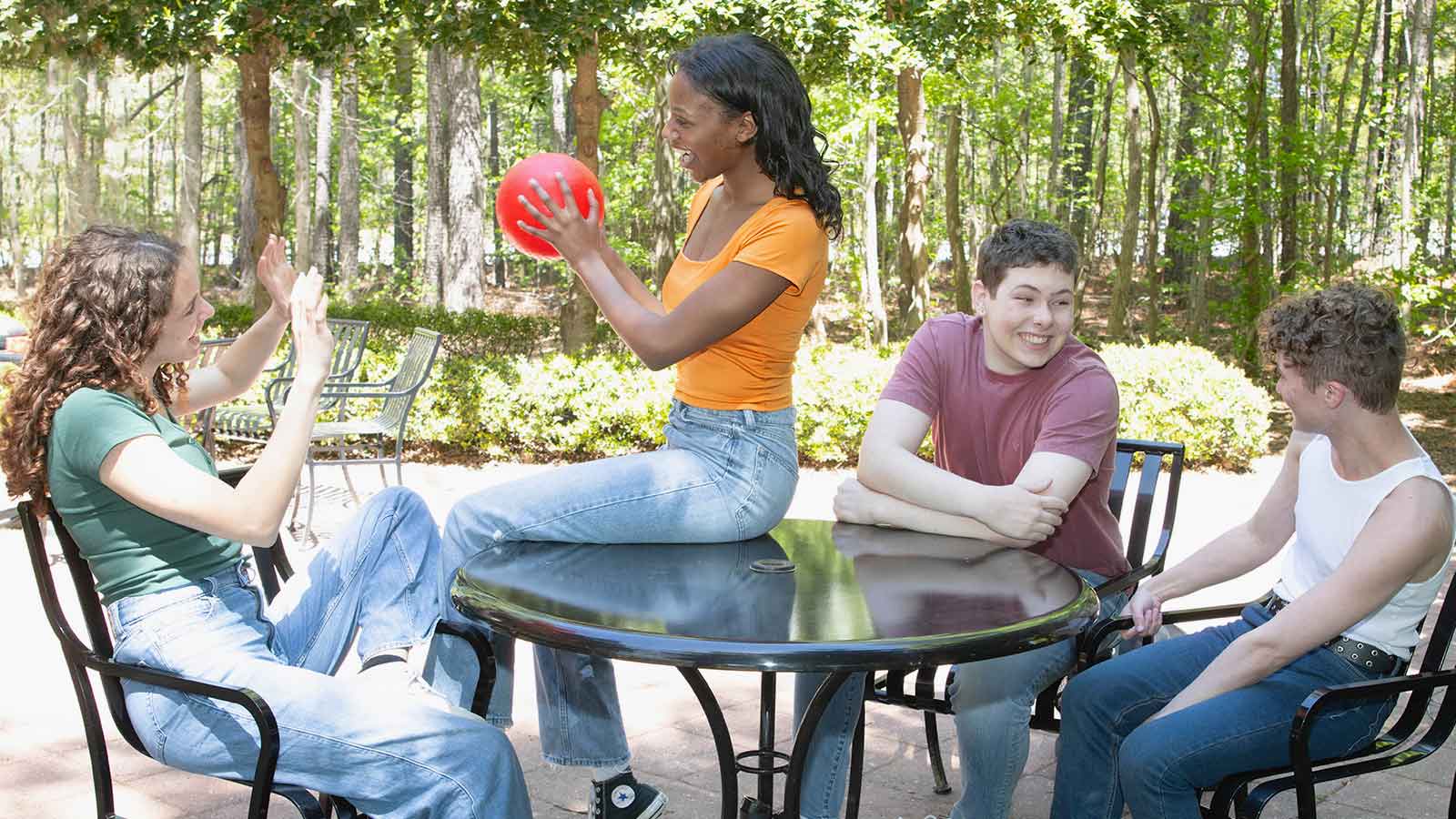 Four teenagers around a table outside having fun and laughing with each other.