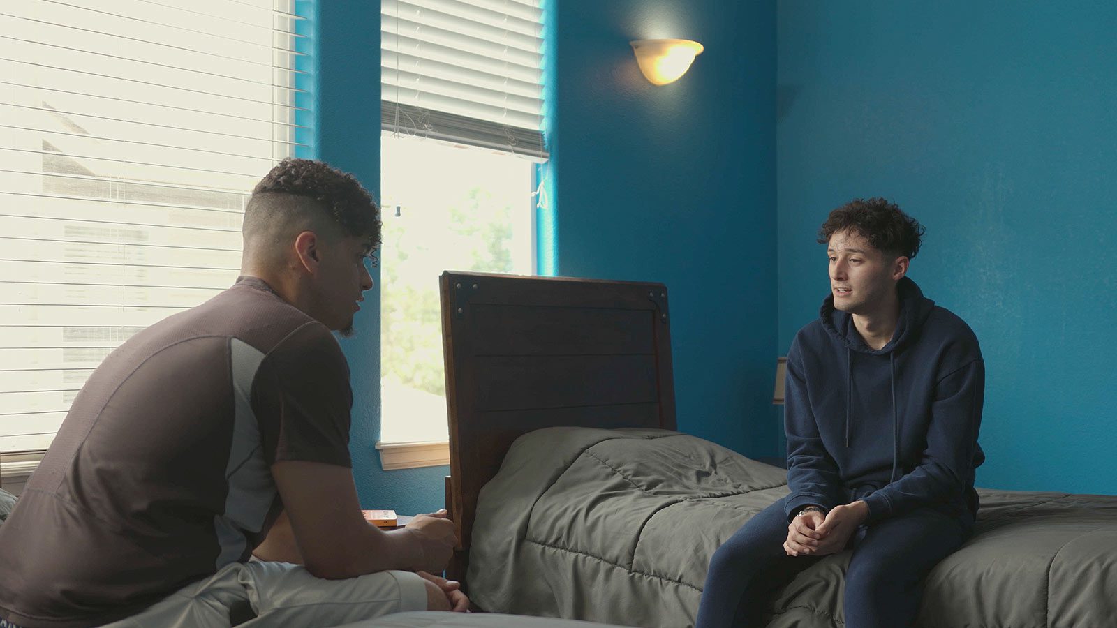 Two men having a conversation in a bedroom.