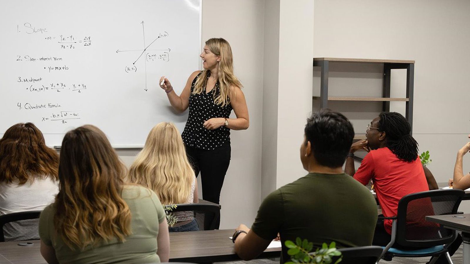 A classroom setting with an instructor teaching and students looking at a whiteboard with mathematical formulas.