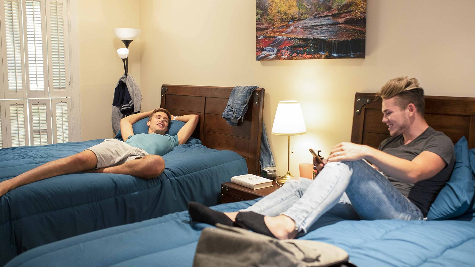 Two young men lounging on beds, relaxing and enjoying activities in a cozy room.