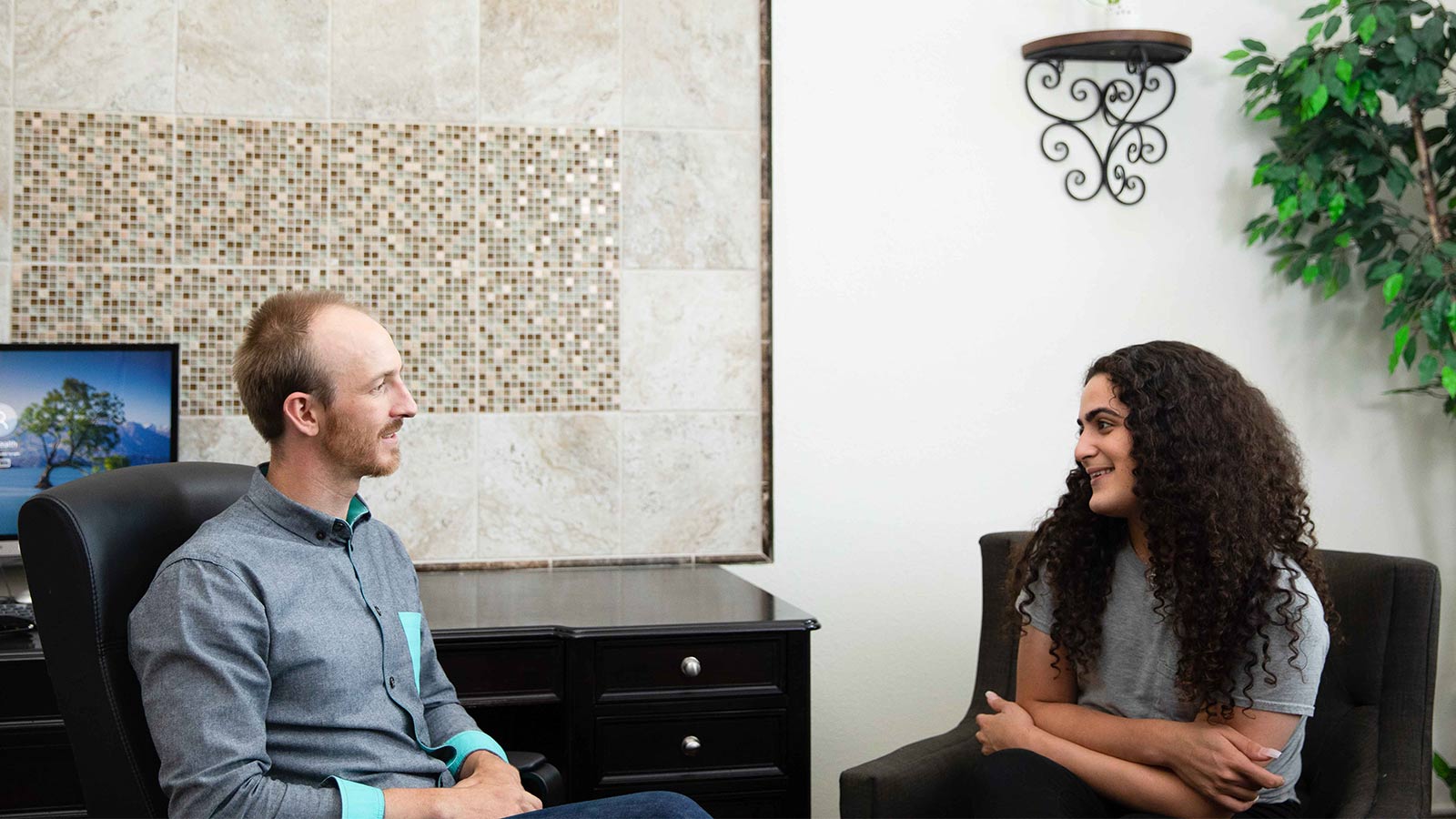 A man and a woman having a conversation in an office with modern furnishings and a decorative tile wall.