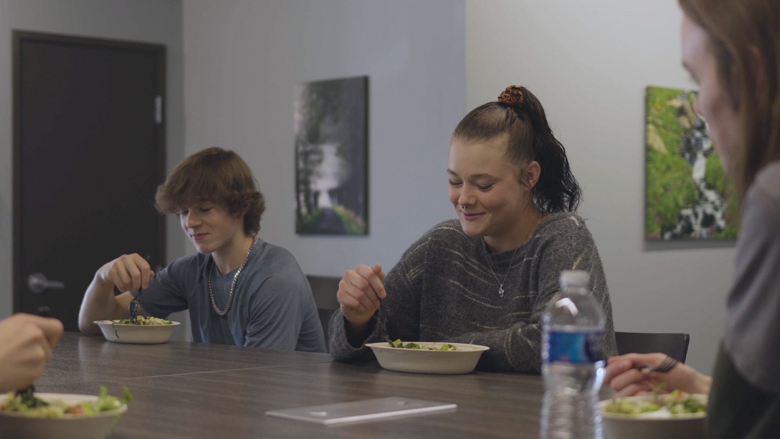 A communal dining area where young individuals are sharing a meal and a conversation at a long table.