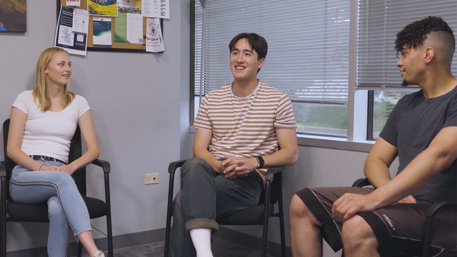 A young man smiling in a group session with other participants in a supportive, open space.