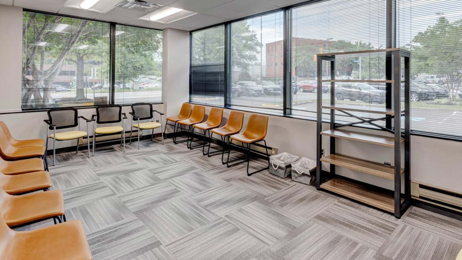 A group therapy room with a row of chairs facing large windows overlooking a parking lot.