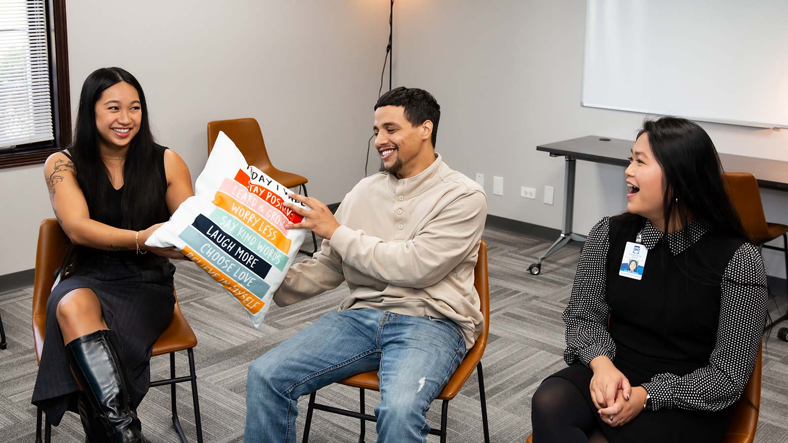 A person holding a motivational pillow laughs with others in a light-filled group room.