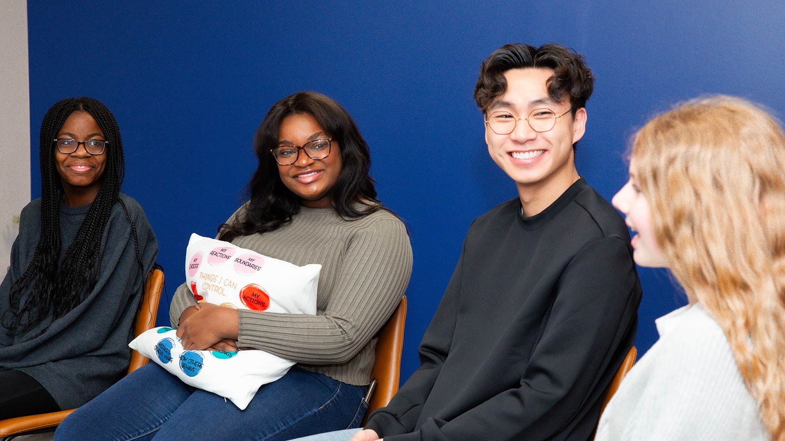 Four people seated in a room with blue walls, smiling and having a conversation.