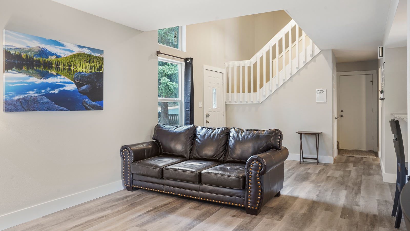 A living area with a large leather sofa, a canvas of a mountain landscape on the wall, and a staircase.