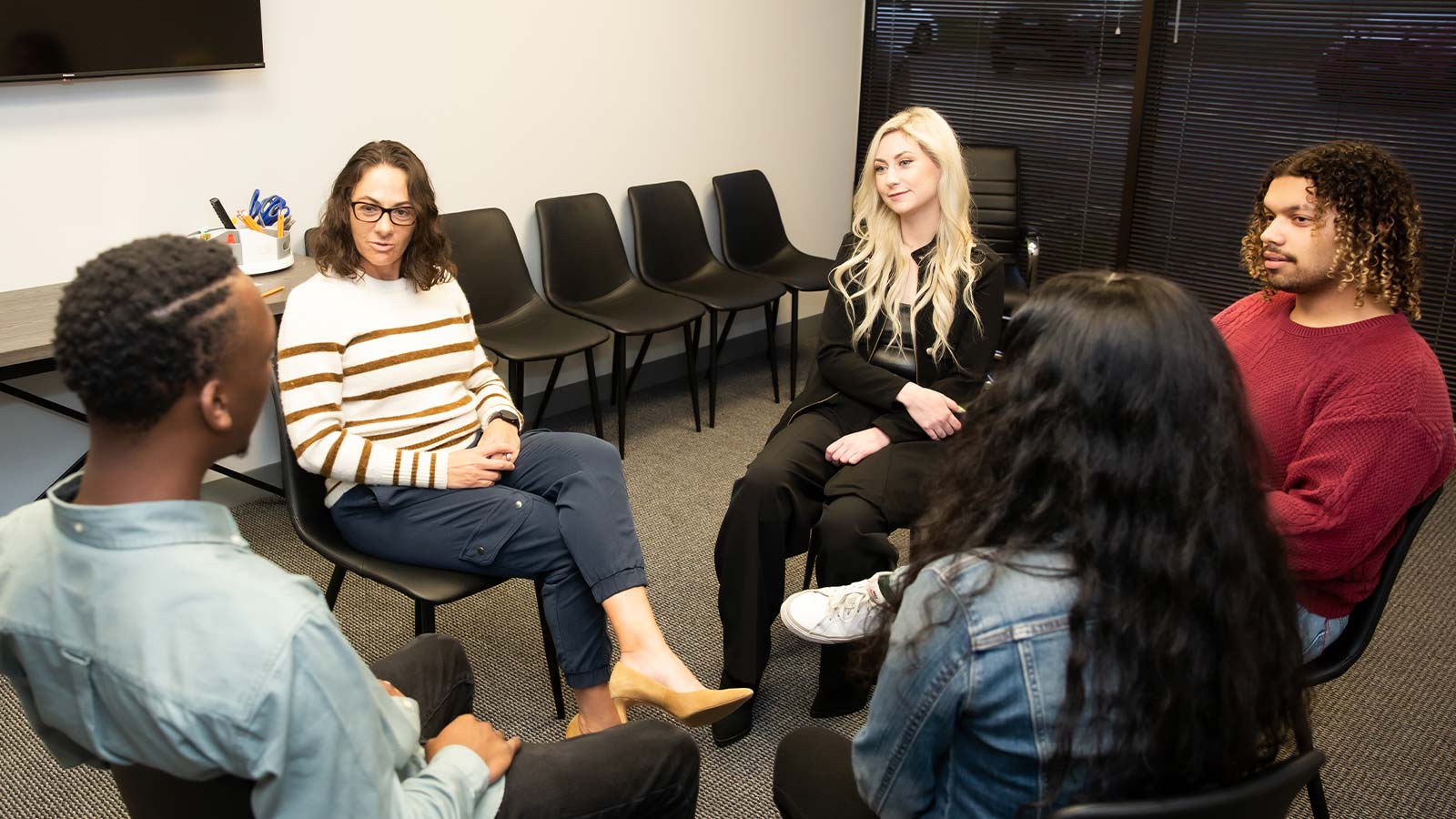 A therapy session with a professional and participants engaging in conversation in a comfortable room.