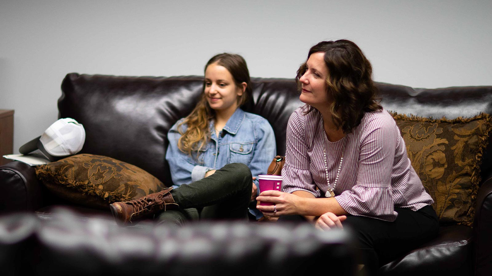 there are two women sitting on a couch talking and drinking