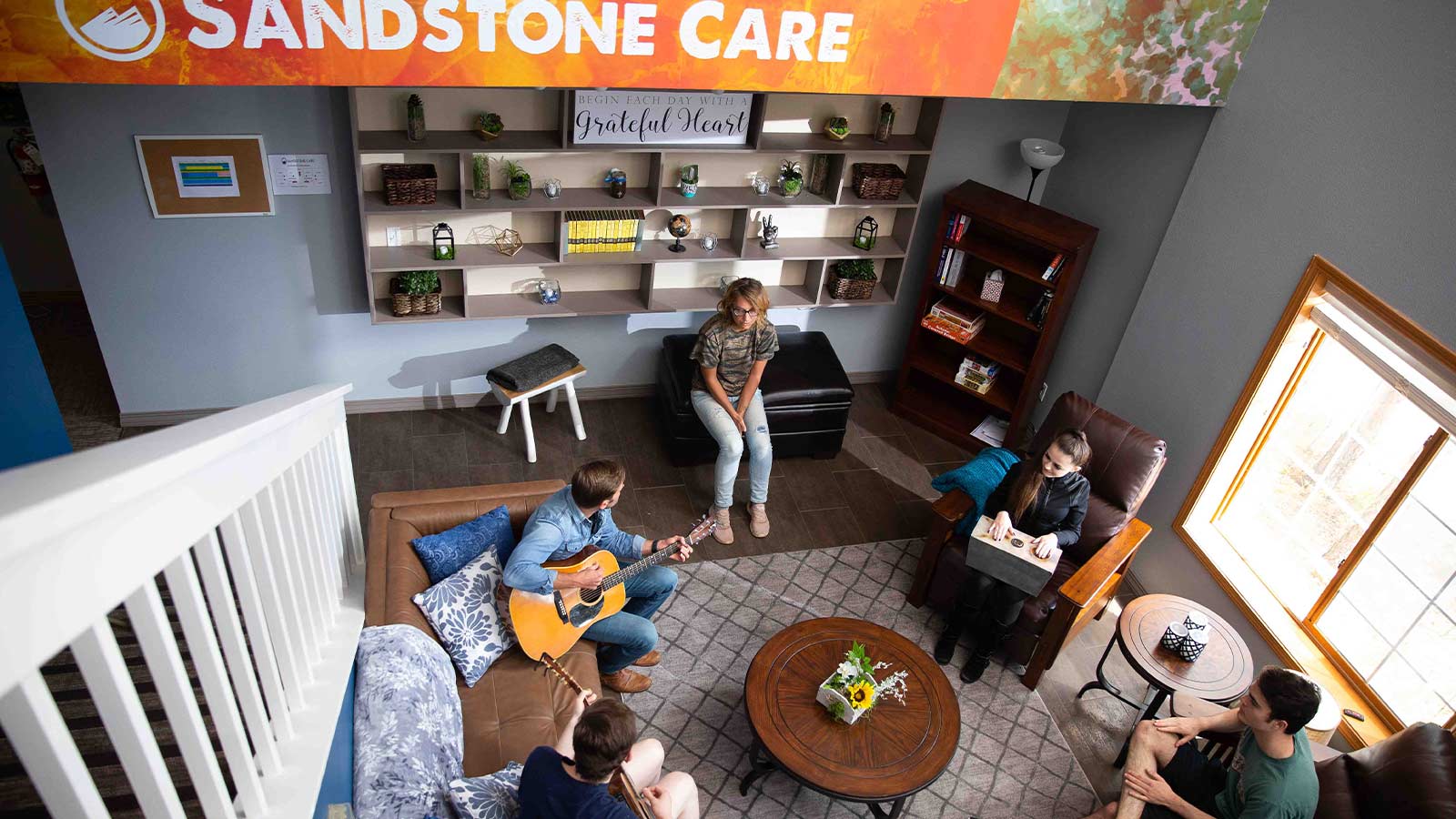 An aerial view of a cozy lounge area with people conversing, featuring mural wall with the text "Sandstone Care."