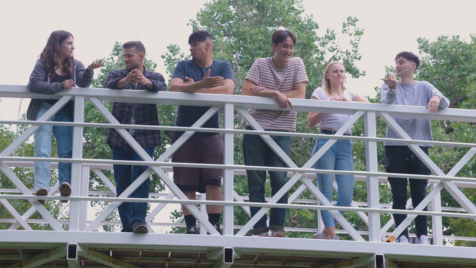 A casual meeting on a bridge outdoors, with a group of young adults engaged in conversation.