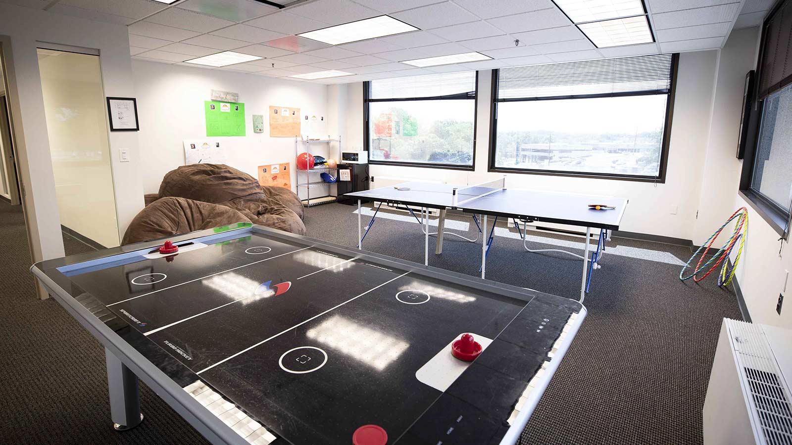 An activity room with an air hockey table and other recreational items, with large windows.